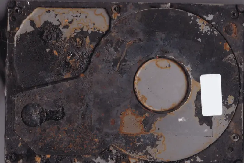 A heavily damaged and burnt hard drive with visible rust and melted components.