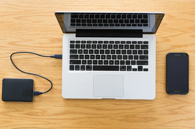 A MacBook, smartphone, and external drive sitting on a table.