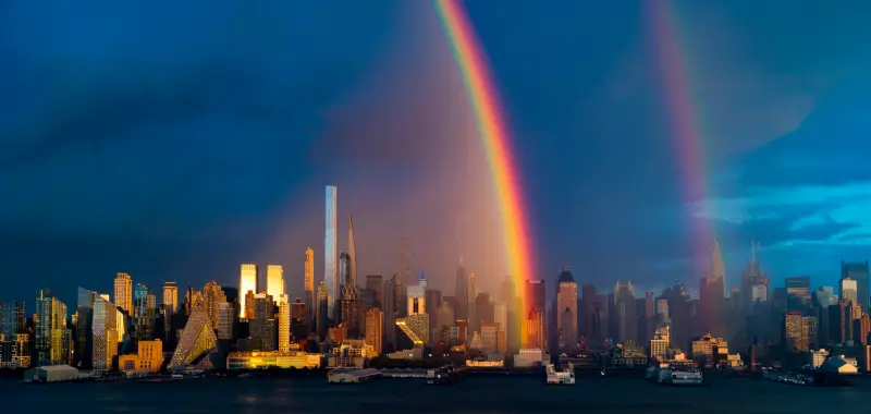 Vibrant rainbow arcing over the Manhattan skyline from the Hudson River.