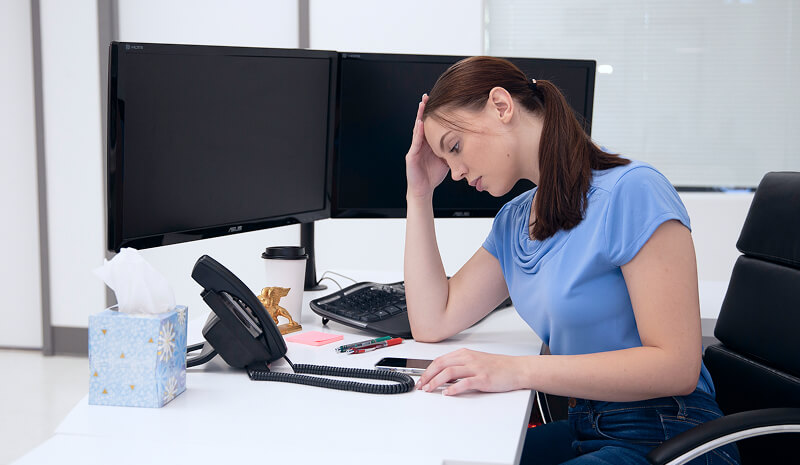 An image of a woman at a desktop with a blank screen.